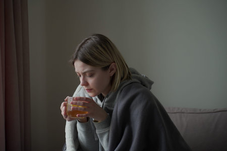 Sick woman drinks tea from a glass in light background