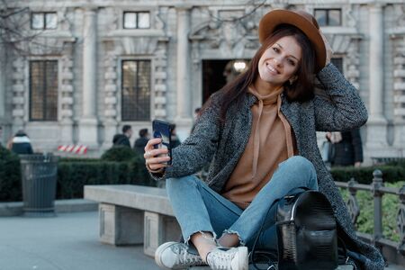 Girl putting her hand on a fashionable brown hat smiles and takes a selfieの写真素材