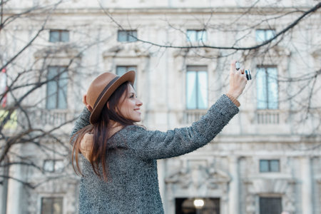 A young brunette girl takes pictures holding a hat with her hand