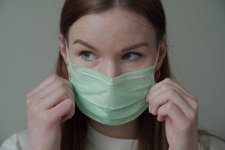 Close up of a beautiful young girl with long red hair in a medical mask. Orvi, coronovirus, acute...