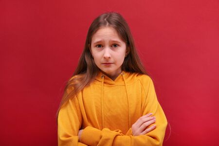 A close-up of a crying girl. A sad girl looks into the camera. Bright red background.の写真素材