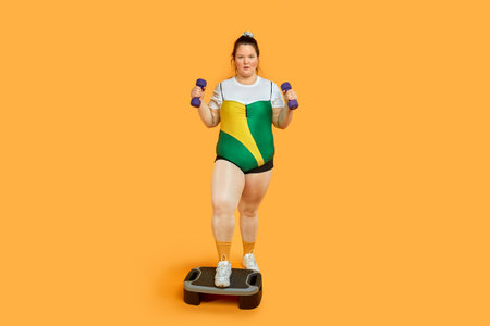 Bright cheerful fat girl is engaged in sports and looks at the camera. Yellow background.