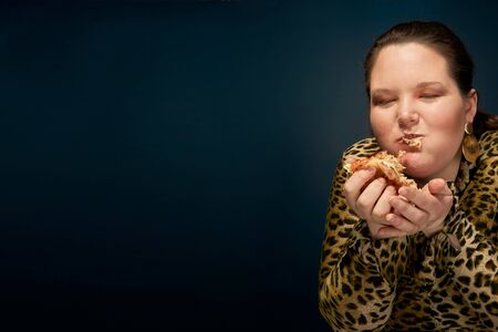 Fat girl in a leopard blouse with a hamburger in her hand. Empty space on the left. Bright makeup. Blue background.の写真素材