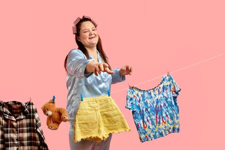 Cheerful beautiful fat girl in blue pajamas hangs clothes after washing, a good and happy wife. Pink background.の写真素材