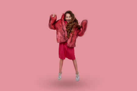 Beautiful young girl dancing in a long pink coat on a pink backgroundの写真素材