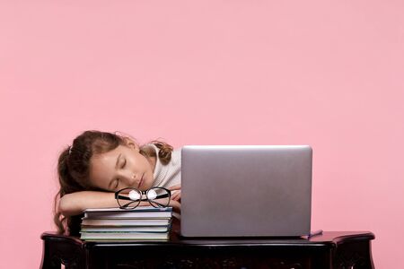 A beautiful young girl, a blonde schoolgirl, fell asleep at the desk on her arm due to a long exhausting study. On a pink backgroundの写真素材