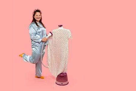 Funny fat girl steams everyday dress. Pink background. One leg is lifted up.の写真素材