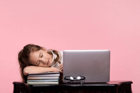 A beautiful young girl, a blonde student, fell asleep on her arm at work on a laptop on a pink backgroundの写真素材