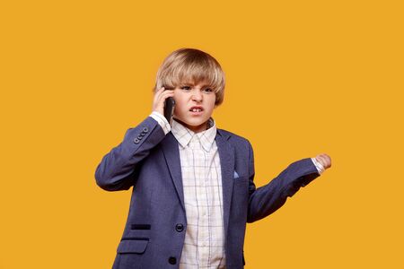 Angry boy talking on the phone. Not a good phone call. Yellow background.の写真素材