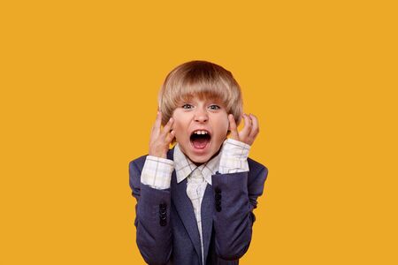 A little handsome blond boy screams with horror and smiles at the camera. Yellow background.の写真素材