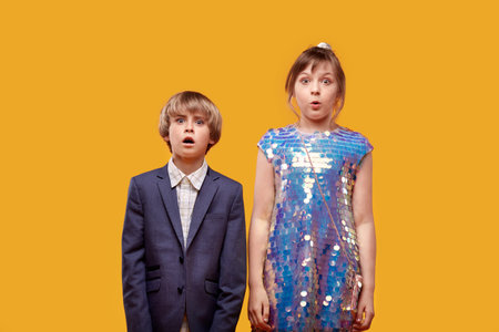 Two surprised cute children in festive clothes with their mouths open. yellow background.