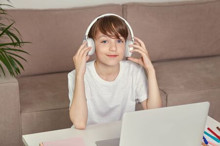 Handsome smiling young guy is studying at home online with headphones on his head. A cozy house.の写真素材