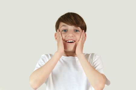 A boy with a surprised expression. Hands near the face. A child in everyday clothes. The white background. Human emotions.の写真素材