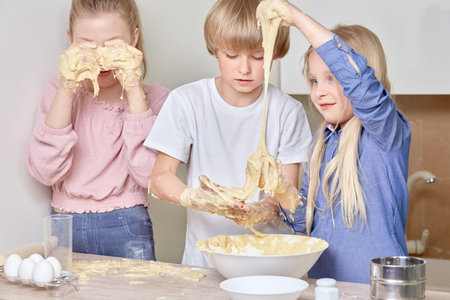 Beautiful cute kids blond siblings helping mom in the kitchen. Children cook cookies.