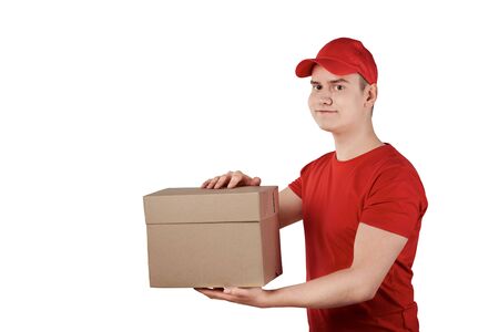 The guy from the delivery service in a cap with a parcel in his hands, white background. The guy in the red uniform.の写真素材