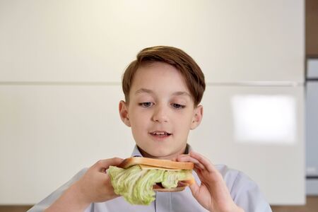 Close-up face of a handsome brunet boy who eats a sandwich. A boy is eating breakfast in front of the school.の写真素材