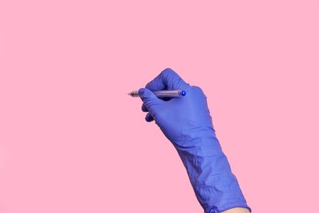 Close-up hand in medical latex gloves writing information with a pen. Isolated pink background.の写真素材