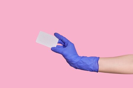 A hand in a surgical glove holds a business card or blank paper isolated on a pink background.の写真素材