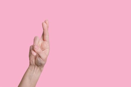 Gesture symbol of good luck, fingers crossed, bright hand on a pink isolated background.の写真素材