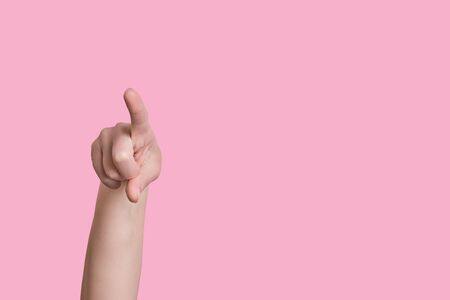 Female beautiful caucasian hand points a finger at the camera. Appeal to the viewer. Isolated on a pink background.の写真素材
