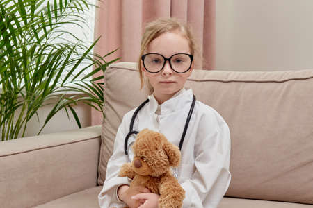 A cute girl put on a doctor uniform and a stethoscope. Holding a cute teddy bear in his hands.の写真素材