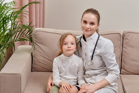 On the sofa is a beautiful female doctor and a blond child. Look at the camera and smile.