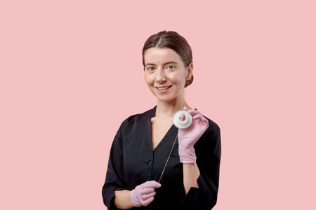 The girl smiles, looks at the camera and holds dental floss in her hands. Pink background.