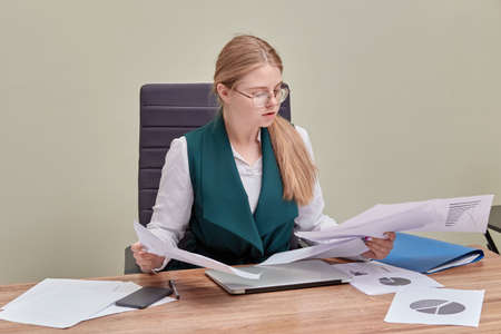 Office work. Beautiful business woman in glasses sitting at a computer parses papers. Office worker.の写真素材