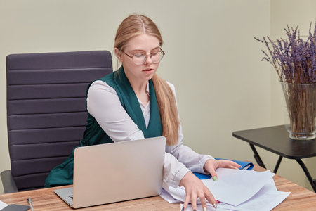 Office work. Young beautiful girl sitting at the computer parses papers. Lavender flowers bouquet in...