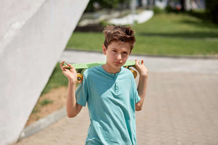 The face of a young handsome brunette guy with a penny skate behind his back and an expressive look. Summer walks. Blurred background.の写真素材
