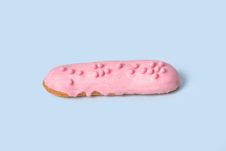 Bright Eclair in pink glaze sprinkled with colorful pink jelly beans, balls. Isolated on a blue...
