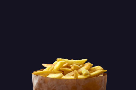 Fries in a craft ecological package on a dark black background. Unhealthy fast food.の写真素材