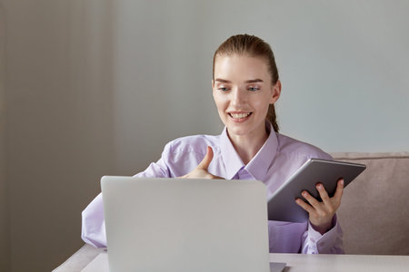 A young woman looks at the laptop screen and shows a thumbs-up gesture. Work during the quarantine....
