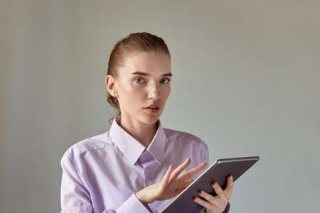 A beautiful young woman uses a tablet and looks at the camera. Beautiful female face with natural makeup.の写真素材