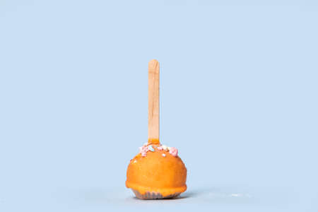 Chocolate holiday dessert in orange glaze. Round pastry on a wooden stick. Dessert for Halloween Blue background.の写真素材