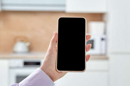 Close-up of a phone with an empty black screen on a light blurry background. Beautiful well-groomed hands.の写真素材