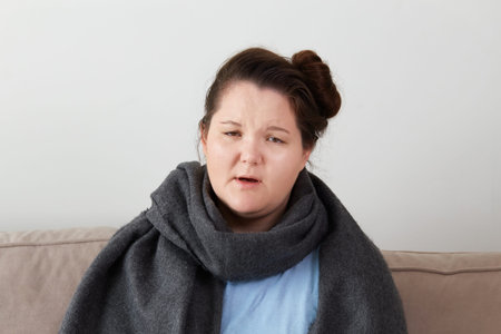 Portrait of a sick young girl, looking at the camera, a warm gray scarf around her neck. Sit at...