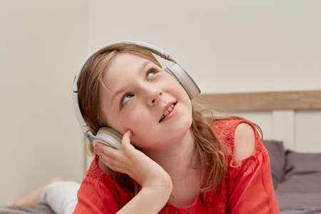 Young beautiful girl in big white headphones, smiling and looking at the camera. Morning in bed.の写真素材