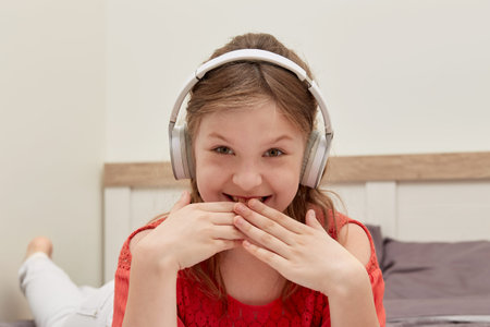 A cute girl is lying in bed, listening to music, laughing and covering her mouth with her hands....