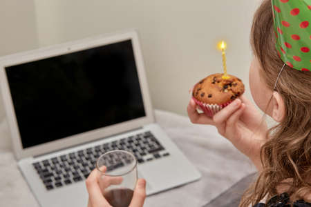 The girl shows the screen a birthday cake with a candle. Talk face to face. The gray notebook. The blurred image of the laptop.の写真素材