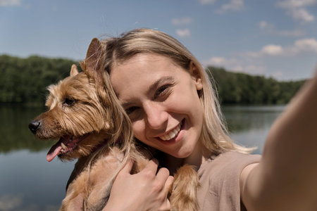 Beautiful blonde woman takes a selfie with her favorite dog. On the background of the lake and...