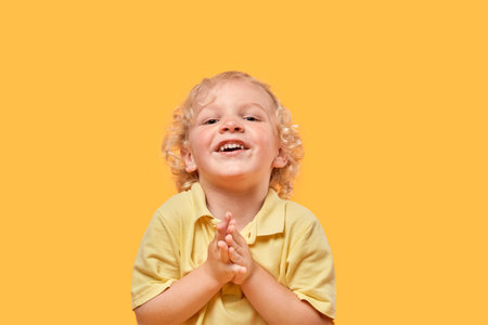 Funny beautiful blond boy on a yellow background looks at the camera. Human emotion.