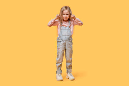 Angry girl in full growth looks at the camera. Clenched fists. Yellow isolated background.の写真素材