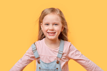 Portrait of a little blonde girl laughing and looking at the camera. Yellow isolated background.