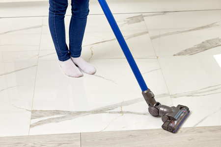 A girl with a vacuum cleaner in her hands is cleaning the house. Light white floor. Home routine....