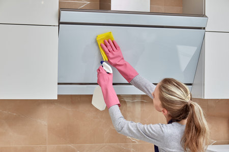 A young beautiful woman cleans to get household chemicals in the kitchen in a can, in latex gloves....