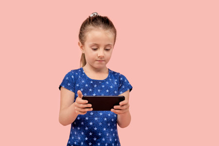 A girl is playing games with a smartphone in her hands. In a blue dress with a small star print....