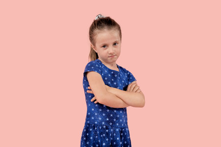 A disgruntled angry girl is upset and looks angrily at the camera in a blue dress. Pink isolated background.の写真素材
