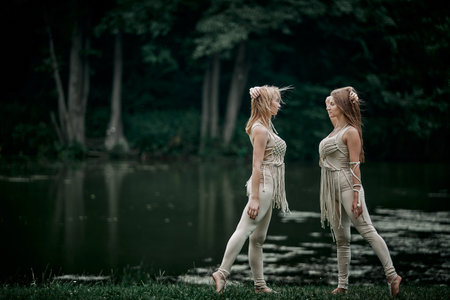 Two young women in a beige dress looking at each other in the nature. There is a large lake behind. The concept of natural cosmetics and harmony with nature. My hair is blowing in the wind.の写真素材