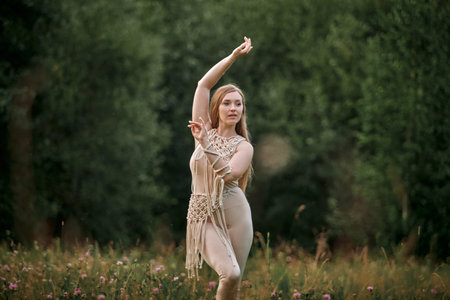 Beautiful young woman doing yoga in nature in summer. Clothing made of eco-friendly materials in beige and macrame.の写真素材
